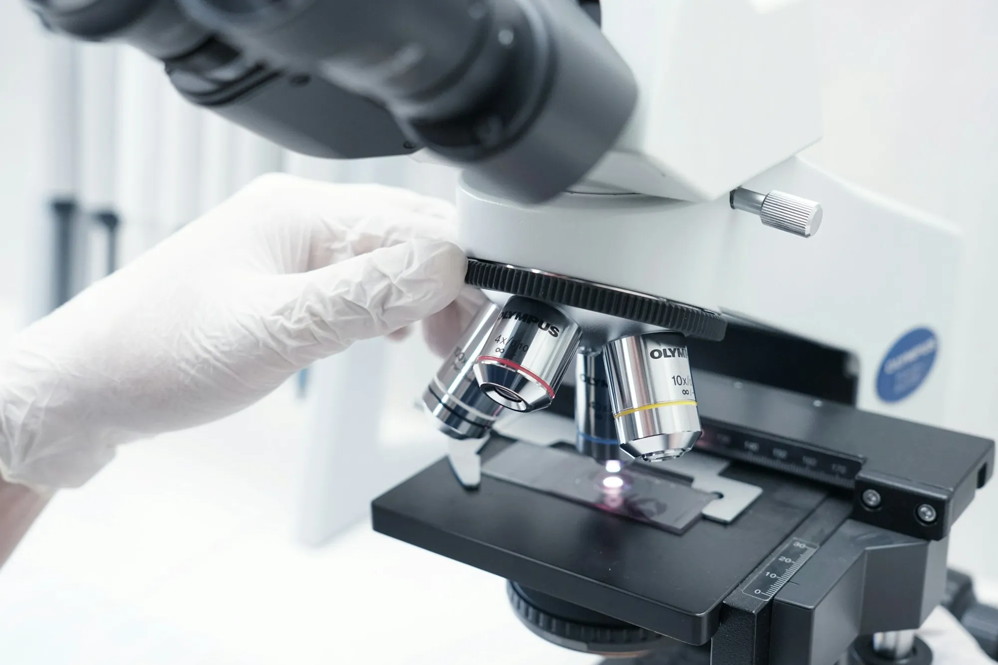 Gloved hand adjusting a sample slide under a microscope